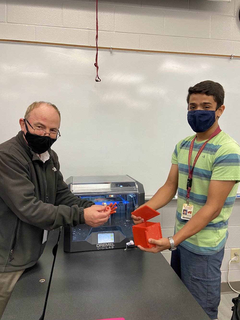 Student and instructor holding 3D printed parts beside a 3D printer